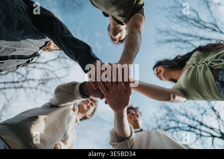 Young friends standing in a circle joining hands outdoors in a park showing unity and teamwork Stock Photo