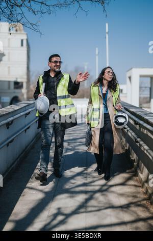 Construction engineers in hi vis vests walking with hard hats and plans on an outdoor site Stock Photo