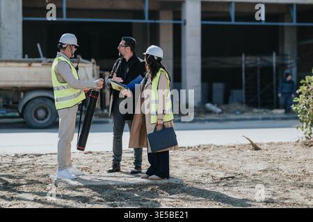 Construction engineers and project managers discussing plans at an urban building site wearing hard hats Stock Photo