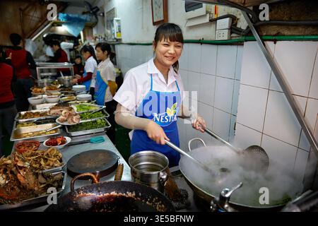 Chefs prepare dishes while working in a busy kitchen in Hanoi. The scene shows food being cooked and served to customers. Stock Photo
