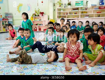 Kids sit on the floor in a classroom in Ho Chi Minh City. They listen to the teacher and engage in learning activities. Stock Photo