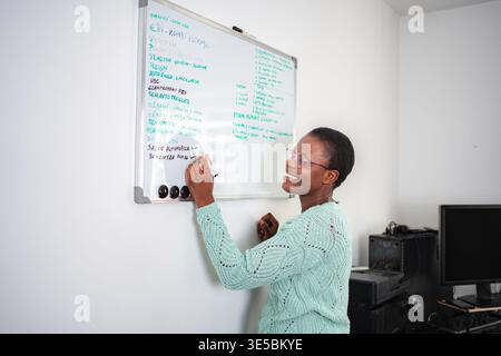 Happy woman writing task list on whiteboard in office Stock Photo