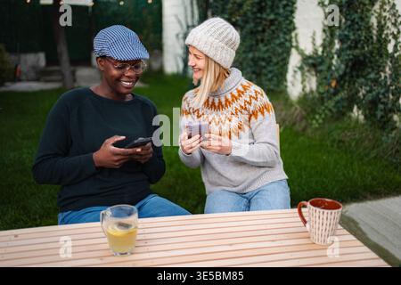 Diverse women friends sitting outdoors laughing using mobile phones Stock Photo
