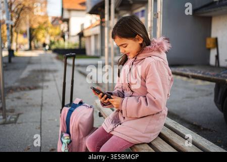 Girl sitting on bench using smartphone waiting for travel Stock Photo