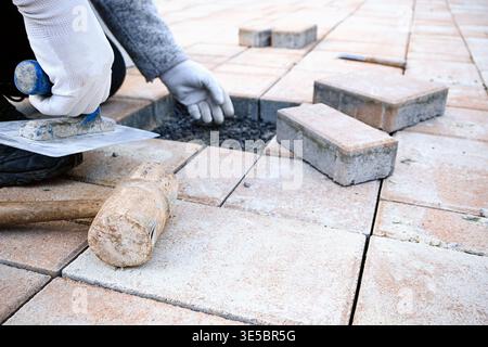 Worker is carefully placing paving stones on a prepared gravel base for a new patio. Stock Photo