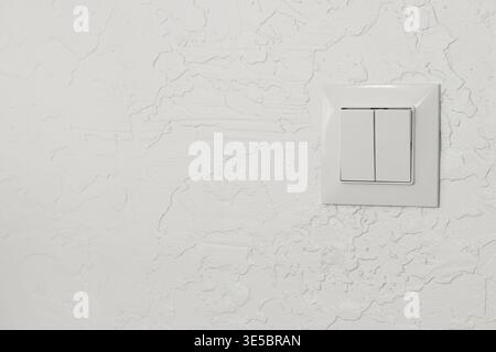 A white light switch plate with two toggle switches mounted on a textured white wall surface, providing a clean and minimalist look Stock Photo