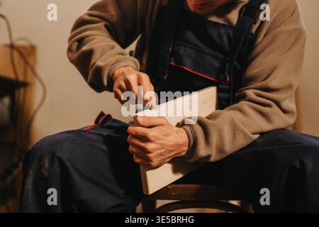 Carpenter shaving a wooden board by hand while sitting in a workshop Stock Photo