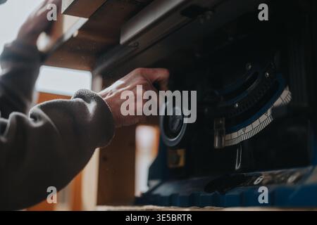 Woodworker adjusting table saw angle with hand in a dusty workshop setting for precision cutting Stock Photo