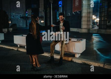 Business colleagues exchanging documents at night in the city with smiling man on bench Stock Photo