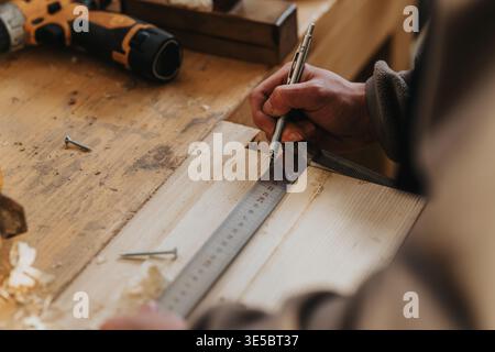 Carpenter measuring and marking a wooden board with a metal ruler in a workshop Stock Photo