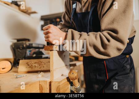 Carpenter planing a wooden plank on a workbench in a workshop showing hands-on woodworking craftsmanship Stock Photo