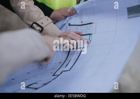 Construction engineers reviewing large blueprint plans together on site while pointing at architectural drawing Stock Photo