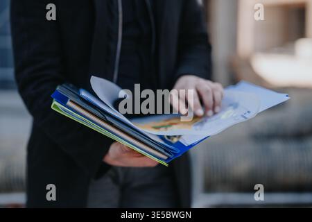 Construction engineer reviewing project plans and documents outdoors while pointing at building drawings Stock Photo