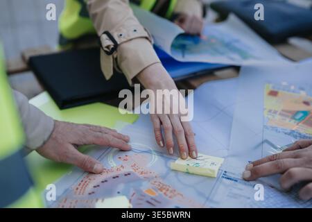 Construction engineers collaborating over blueprints and site plans during on-site planning meeting Stock Photo