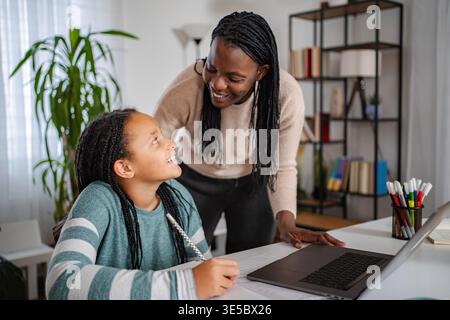 Mother helping daughter with homework using laptop at home Stock Photo