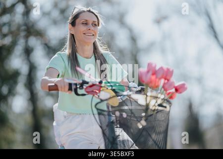 Mother and daughter enjoying a bike ride with tulips in the basket on a sunny spring day Stock Photo