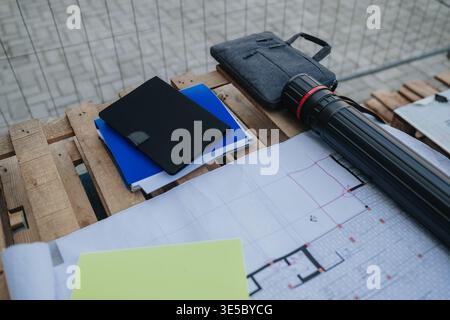Architectural plans and notebooks on a wooden pallet with blueprint tube at construction site Stock Photo