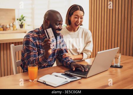 Cheerful man and woman are shopping online by using laptop at home. Stock Photo