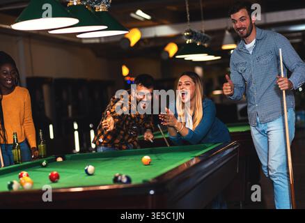 Four smiling friends in bar playing billiard together. Stock Photo
