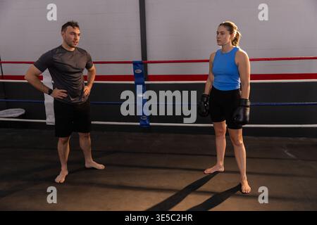Male coach and female boxer standing in ring wearing gloves and blue top, red or white or blue ropes Stock Photo
