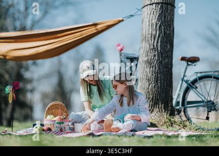 Mom and daughter enjoying a relaxed outdoor picnic under a tree with a bicycle nearby Stock Photo