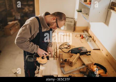 Carpenter sanding wooden board in workshop using an electric sander on workbench Stock Photo