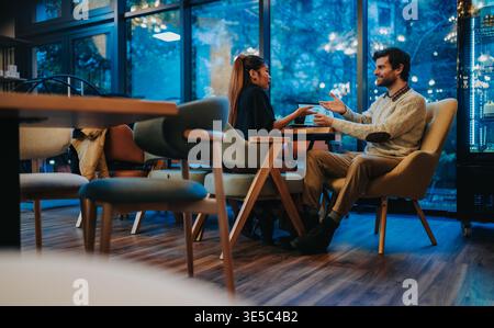 Business meeting between two colleagues chatting over coffee in a modern cozy cafe in the evening Stock Photo