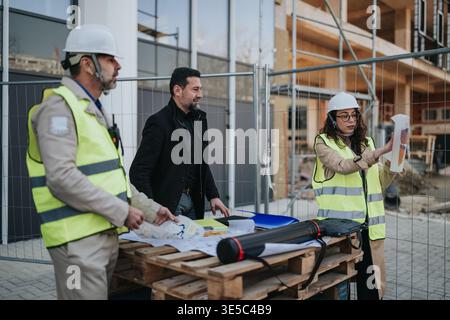 Construction engineers reviewing plans at an active building site with hard hats and high-visibility vests Stock Photo