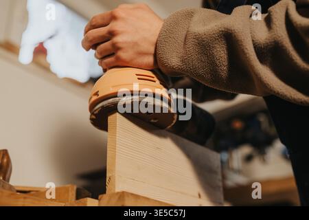 Carpenter sanding wooden board by hand with electric sander in workshop close-up Stock Photo