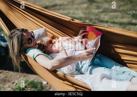 Mother and daughter relaxing in a hammock reading a colorful book together outdoors Stock Photo