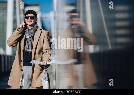 Businessman talking on phone while walking in city with coat scarf and papers in hand Stock Photo