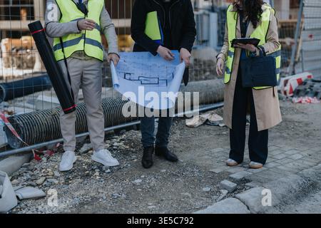 Construction engineers reviewing blueprints at an urban building site wearing safety vests Stock Photo