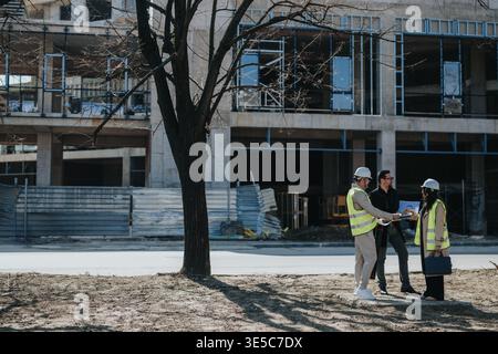 Construction engineers in safety vests discussing blueprints at an urban building site Stock Photo