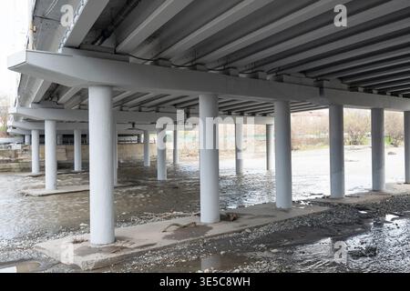 Reinforced concrete pillars and beams supporting a highway bridge over a river. View under a massive concrete bridge structure with multiple columns s Stock Photo