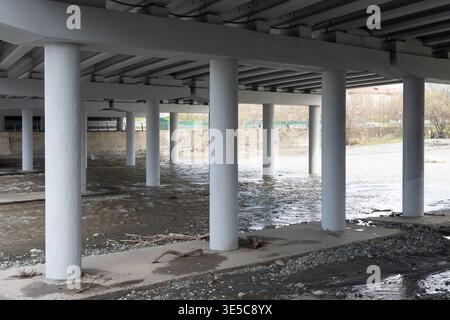View under a massive concrete bridge structure with multiple columns standing in the water.  Reinforced concrete pillars and beams supporting a highwa Stock Photo