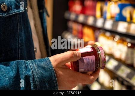 Man closely inspecting product label details. Male shopper scrutinizing ingredients on container in store. Male customer carefully reviewing Stock Photo