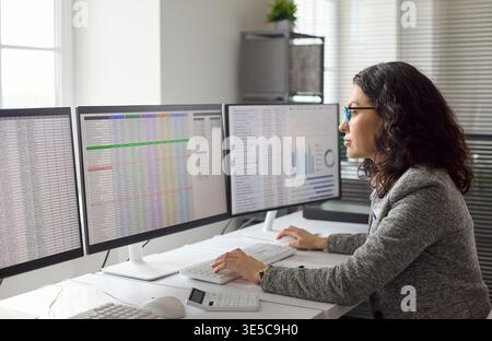 Female financial analyst reviewing spreadsheets on dual monitor workstation Stock Photo
