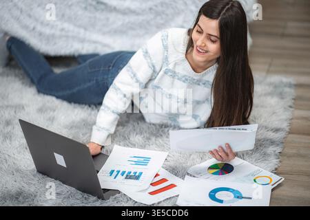 Woman lying on rug analyzing financial data using laptop Stock Photo