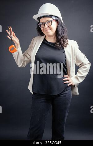 Woman professional wearing hard hat and glasses, confidently holding a tape measure and pencil Stock Photo