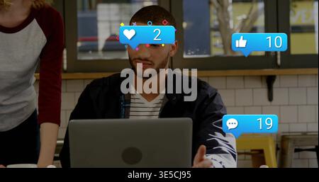 Working man in striped T-shirt, dark jacket typing on silver laptop at cafe with floating reactions Stock Photo