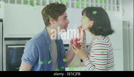 Sipping couple leaning toward plastic cup in home kitchen, holding red smoothie and striped straws Stock Photo