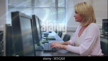 Typing woman in pink cardigan at computer lab desk, using monitors, keyboards, copy space Stock Photo