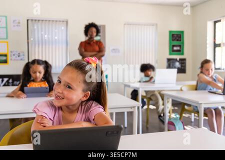 African American teacher watching school age children using tablets and laptop in classroom Stock Photo