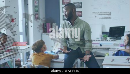 Talking seated teacher wearing light green shirt gesturing to students in classroom, with notebooks Stock Photo