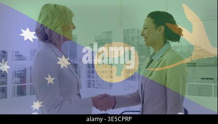Shaking hands two women in suits greeting across table at office windows, flag overlay visible Stock Photo