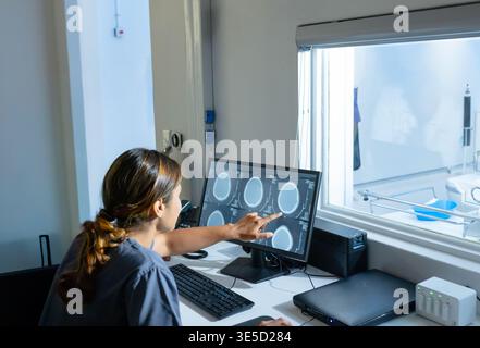 African American woman in dark scrubs pointing at brain scan monitor at radiology control room. Neuroimaging, workstation, hospital, clinical, diagnos Stock Photo