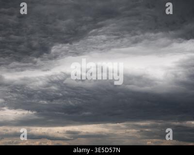 Dark, heavy storm clouds swirl across the sky, layered in deep gray tones. Tense moody atmosphere before rain and thunder. Stock Photo