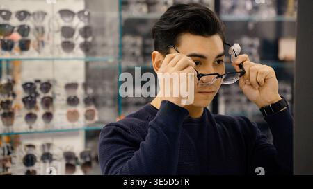 Man trying on stylish black glasses in optics Stock Photo