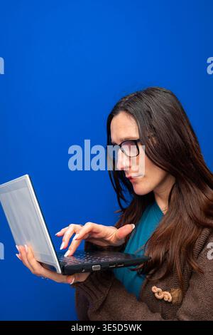 Woman wearing eyeglasses focusing on a small laptop, typing on the keyboard. Representing remote work, education, and technology Stock Photo