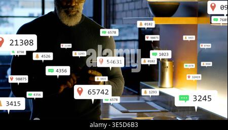 Checking senior man in dark knit sweater holding smartphone in workspace kitchen seeing alerts Stock Photo